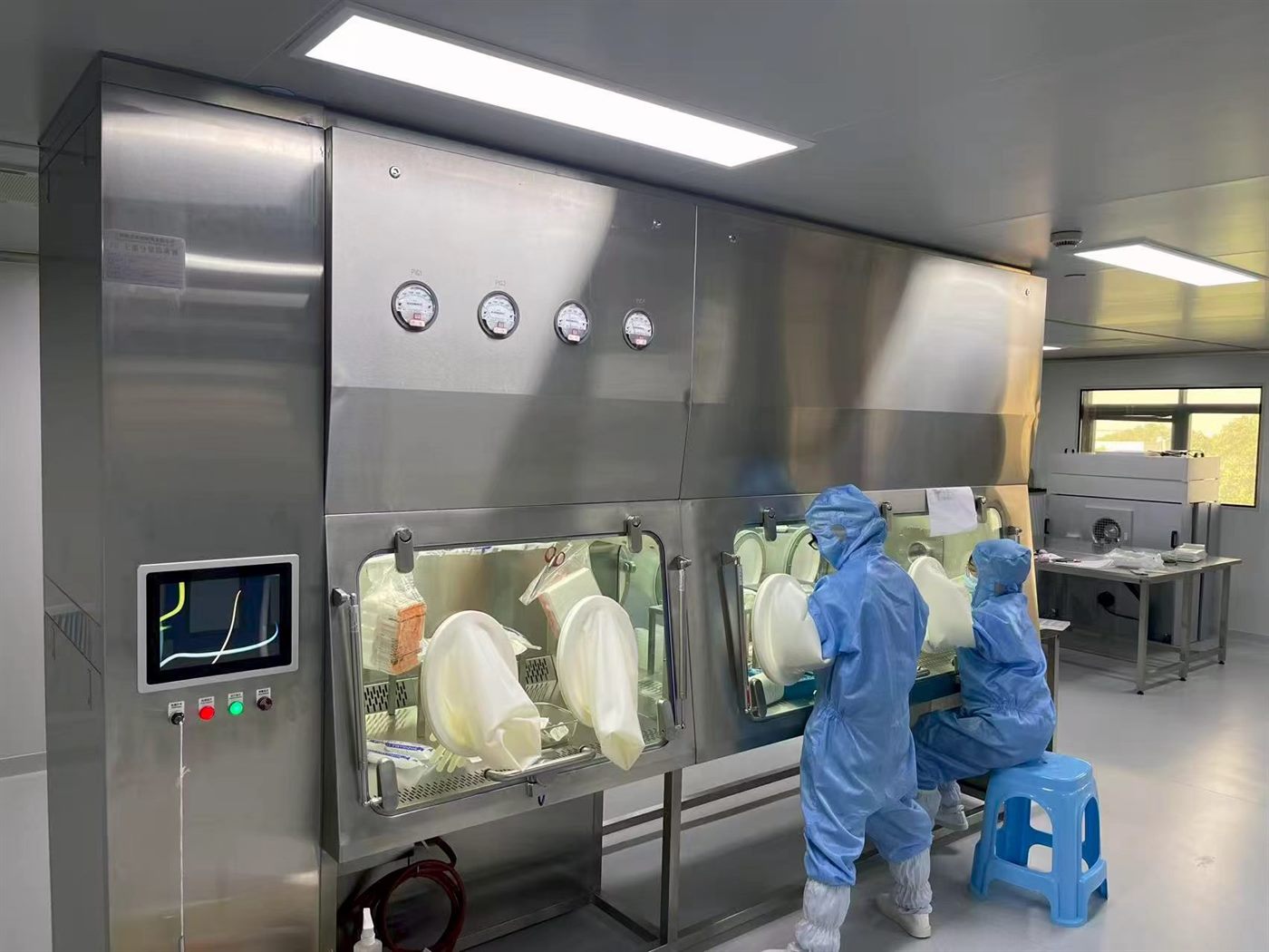 Operators working through the glove ports of a Fenggu rigid isolator (stainless-steel glovebox), the physical barrier separating them from the potent material